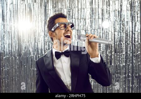 Junger Mann im Smoking und Schleife, der Mikrofon hält und Lieder auf der Karaoke-Party singt Stockfoto