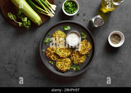 Vegetarische Gemüsezucchini mit Sauce auf Teller auf dunklem Steinhintergrund. Draufsicht, flach Stockfoto