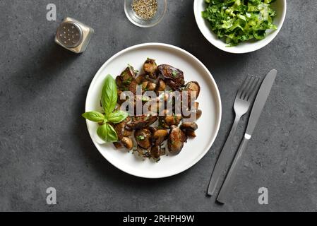 Gebratene Hühnerleber mit Pilzen auf weißem Teller auf dunklem Steinhintergrund. Draufsicht, flach Stockfoto