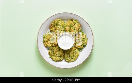 Vegetarische Gemüsezucchini-Pfannkuchen mit Sauce auf Teller auf grünem Hintergrund mit Kopierraum. Draufsicht, flach Stockfoto