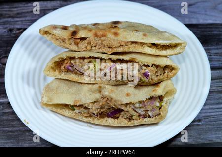 Ein flaches Brot mit pürierten Fava-Bohnen, gemischt mit Öl, Sesam-Tahini, Kreuzkümmel, Gewürzen, Scheiben Chilischeffer und Zwiebeln, selektiver Fokus auf traditionellen Pop Stockfoto