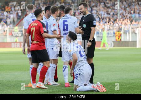 18. August 2023, Hessen, Wiesbaden: Fußball: 2. Bundesliga, SV Wehen Wiesbaden - Karlsruher SC, Spieltag 3, BRITA Arena. Nach einem Foul eines Wehenspielers auf Paul Nebel (2. Von rechts) des Karlsruher SC fordern die Karlsruher Spieler vom Schiedsrichter Wolfgang Haslberger eine gelbe Karte. Foto: Jürgen Kessler/dpa - WICHTIGER HINWEIS: Gemäß den Anforderungen der DFL Deutsche Fußball Liga und des DFB Deutscher Fußball-Bund ist es verboten, im Stadion und/oder im Spiel aufgenommene Fotos in Form von Sequenzbildern und/oder videoähnlichen Fotoserien zu verwenden oder zu verwenden. Stockfoto