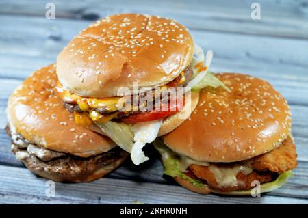 Haufen Sesambrötchen mit frittierten panierten Hähnchenfilet-Pattys, knackigem Salat, Schmelzkäse, Zwiebeln und Sauce, saftigem, dickem, doppeltem Rinderpatty mit Chees Stockfoto