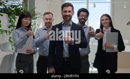 Gruppe glückliche professionelle vielfältige Geschäftsmänner und Geschäftsfrauen lächelnde Mitarbeiter mit Teamleiter zeigen Daumen nach oben Stimme gutes Zeichen Blick auf die Kamera in Stockfoto