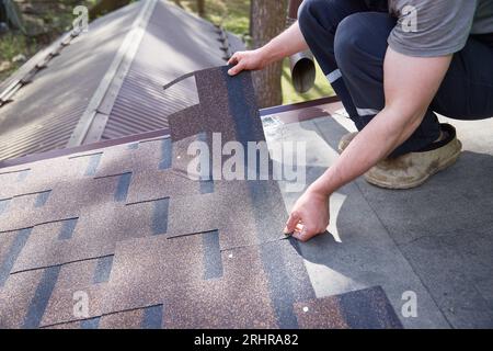 Eine Nahaufnahme der Hände des Meisters auf dem Dach enthält flexible Fliesen Stockfoto