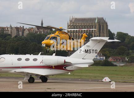 Ein AW-169-Rettungswagen des Kent Surrey Sussex Trust verlässt den Brighton City Airport mit einem Cessna 510 Citation Business Jet im Vordergrund. Stockfoto