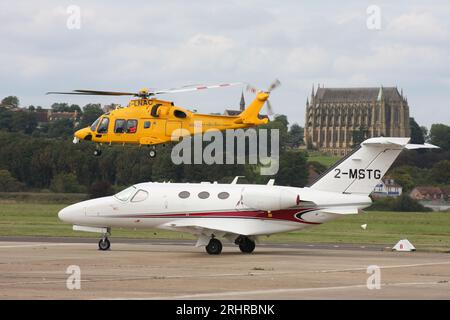 Ein AW-169-Rettungswagen des Kent Surrey Sussex Trust verlässt den Brighton City Airport mit einem Cessna 510 Citation Business Jet im Vordergrund. Stockfoto