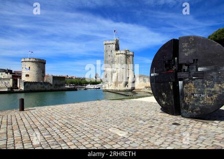 Die Tour Saint-Nicolas und die Tour de La Chaine am Eingang zum Alten Hafen. Skulptur zu Ehren von Michel Crepeau, dem ehemaligen Bürgermeister von La Rochelle. La Rochelle, Charente Maritime, Frankreich Stockfoto