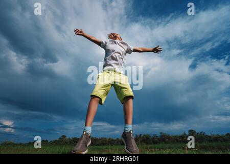 Glücklicher Junge, der auf dem Feld auf blauem Himmelshintergrund springt Stockfoto