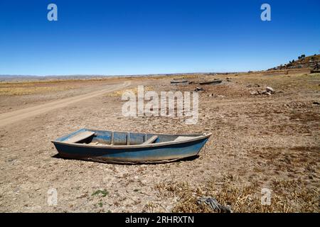 Titicacasee, BOLIVIEN; 18. August 2023: Hölzerne Ruderboote am ausgetrockneten Ufer der Cohana Bay am inneren See / Huiñay Marka (der kleinere Teil des Titicacasees) in der Nähe des Dorfes Cohana (im Hintergrund). Die Wasserstände im Titicacasee nähern sich dem Rekordtief von 1996, dem niedrigsten seit der Aufnahme von Aufzeichnungen durch den bolivianischen Wetterdienst (Senhami) im Jahr 1974. Viele geben dem Klimawandel die Schuld; die letzten Jahre waren trockener als normal, und El Niño verstärkt sich derzeit im Pazifischen Ozean vor Südamerika. Stockfoto