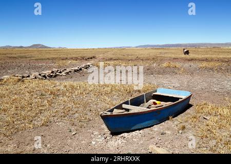 Titicacasee, BOLIVIEN; 18. August 2023: Hölzernes Ruderboot am ausgetrockneten Ufer der Cohana Bay am inneren See / Huiñay Marka (der kleinere Teil des Titicacasees) in der Nähe des Dorfes Cohana. Die Wasserstände im Titicacasee nähern sich dem Rekordtief von 1996, dem niedrigsten seit der Aufnahme von Aufzeichnungen durch den bolivianischen Wetterdienst (Senhami) im Jahr 1974. Viele geben dem Klimawandel die Schuld; die letzten Jahre waren trockener als normal, und El Niño verstärkt sich derzeit im Pazifischen Ozean vor Südamerika. Stockfoto