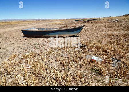 Titicaca-See, BOLIVIEN; 18. August 2023: Ein hölzernes Ruderboot und totes Totora-Schilf am ausgetrockneten Ufer der Cohana-Bucht am inneren See/Huiñay Marka (der kleinere Teil des Titicaca-Sees) in der Nähe des Dorfes Cohana. Die Wasserstände im Titicacasee nähern sich dem Rekordtief von 1996, dem niedrigsten seit der Aufnahme von Aufzeichnungen durch den bolivianischen Wetterdienst (Senhami) im Jahr 1974. Viele geben dem Klimawandel die Schuld; die letzten Jahre waren trockener als normal, und El Niño verstärkt sich derzeit im Pazifischen Ozean vor Südamerika. Stockfoto