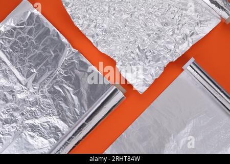 Verschiedene Rollen Aluminiumfolie auf orangem Hintergrund, flach liegend Stockfoto