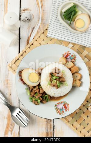 Top View Nasi Bakmoy, gekochter Reis serviert mit gebratenem Hühnchen, Brühe, geschnittenen Scallions, halb gekochtem Ei und Shrimp-Reiskuchen. Stockfoto