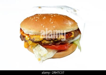 Ein saftiges, dickes, doppeltes Rinderpatty mit Käse, der mit Sauce bedeckt ist, knackigem Salat, frischen Tomaten, Zwiebeln und Gurken in einem großen Sesambrötchen, einem Rindfleisch Stockfoto