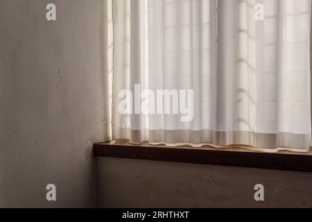 Selektiver Fokus auf Innenansicht des lichtdurchlässigen weißen Vorhangs mit durchgehendem Sonnenlicht und dem Boden des weißen Vintage-Zimmers aus Holz. Stockfoto