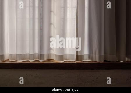 Selektiver Fokus auf Innenansicht des lichtdurchlässigen weißen Vorhangs mit durchgehendem Sonnenlicht und dem Boden des weißen Vintage-Zimmers aus Holz. Stockfoto