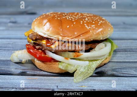 Ein saftiges, dickes, doppeltes Rinderpatty mit Käse, der mit Sauce bedeckt ist, knackigem Salat, frischen Tomaten, Zwiebeln und Gurken in einem großen Sesambrötchen, einem Rindfleisch Stockfoto