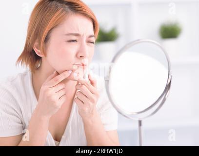 Junge Frau, die Pickel zusammendrückt, um sie aus dem Gesicht zu entfernen. Stockfoto