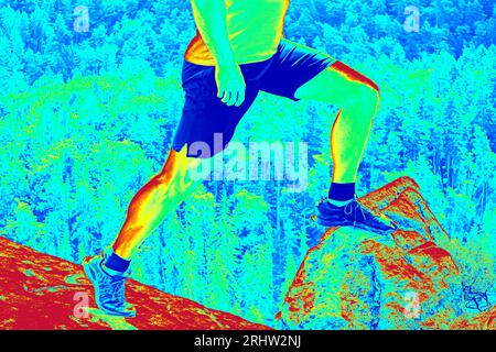 Lange Beine in Wanderschuhen auf dem Gipfel. Wandern in Sandsteinfelsen. Fantastisches Thermografie-Foto der hügeligen Landschaft. Stockfoto