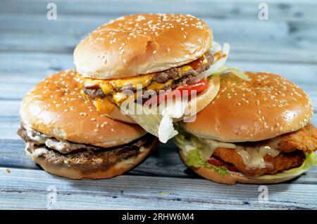 Haufen Sesambrötchen mit frittierten panierten Hähnchenfilet-Pattys, knackigem Salat, Schmelzkäse, Zwiebeln und Sauce, saftigem, dickem, doppeltem Rinderpatty mit Chees Stockfoto