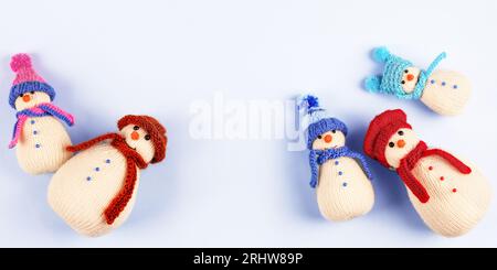 Gestrickte Schneemänner in bunten Hüten und Tüchern auf blauem Hintergrund. Konzept von Weihnachten, Neujahr und Wintermärchen. Kreatives Stricken von Spielzeug für Stockfoto