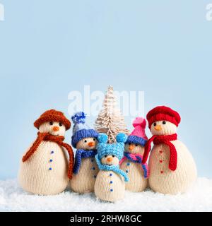 Gestrickte Schneemänner in bunten Hüten und Tüchern auf blauem Hintergrund. Konzept von Weihnachten, Neujahr und Wintermärchen. Kreatives Stricken von Spielzeug für Stockfoto