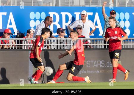 18. August 2023, Hessen, Wiesbaden: Fußball: 2. Bundesliga, SV Wehen Wiesbaden - Karlsruher SC, Spieltag 3, BRITA Arena. Nach dem Tor für 1:0 treffen sich Torschütze Hyunju Lee (SV Wehen Wiesbaden, 20), Ivan Prtajin (SV Wehen Wiesbaden, 18) und lasse Günther (SV Wehen Wiesbaden, 29) zum Feiern. Foto: Jürgen Kessler/dpa - WICHTIGER HINWEIS: Gemäß den Anforderungen der DFL Deutsche Fußball Liga und des DFB Deutscher Fußball-Bund ist es verboten, im Stadion und/oder im Spiel aufgenommene Fotos in Form von Sequenzbildern und/oder videoähnlichen Fotoserien zu verwenden oder zu verwenden. Stockfoto