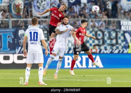 18. August 2023, Hessen, Wiesbaden: Fußball: 2. Bundesliga, SV Wehen Wiesbaden - Karlsruher SC, Spieltag 3, BRITA Arena. Marcus Mathisen (SV Wehen Wiesbaden, 24), Fabian Schleusener (Karlsruher SC, 24) und Robin Heußer (SV Wehen Wiesbaden, 7) steigen gleichzeitig für einen Kopfball hoch. Foto: Jürgen Kessler/dpa - WICHTIGER HINWEIS: Gemäß den Anforderungen der DFL Deutsche Fußball Liga und des DFB Deutscher Fußball-Bund ist es verboten, im Stadion und/oder im Spiel aufgenommene Fotos in Form von Sequenzbildern und/oder videoähnlichen Fotoserien zu verwenden oder zu verwenden. Stockfoto