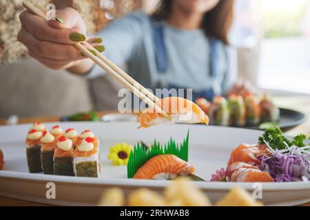 Hände, Essstäbchen und Frau mit Sushi im Restaurant, gutes Essen und Essen im Café. Lachs, Stock und Person auf Fisch, Fleisch und Tempura Essen in Stockfoto