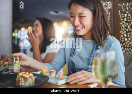 Japanische Frau, Restaurant und essen Sushi mit Lächeln, Essstäbchen und begeistert für feine Speisen auf der Party. Asiatische Freunde, Fisch und gesund mit Kultur Stockfoto