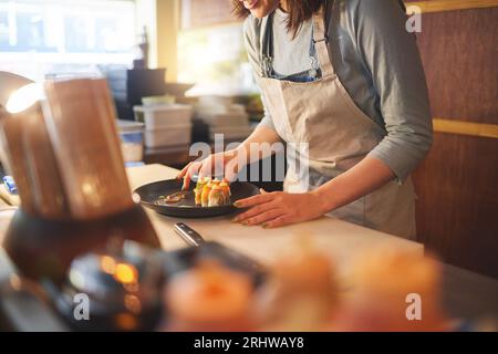 Sushi-Koch, Restaurant und fertig in der Küche mit Händen, Service oder Teller auf dem Tisch, Job oder Catering. Kleine Unternehmen, Fast Food und Kochen im Café Stockfoto