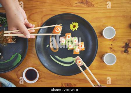 Essstäbchen, Hand und Essen Sushi und Essen in einem Restaurant für Ernährung am Tisch. Über hungrige Menschen mit Holzstöcken und Sojasauce zum Essen Stockfoto