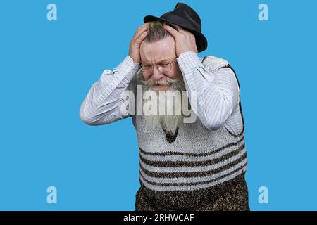 Alter Rentner mit langem Bart, der schreckliche Kopfschmerzen hat. Leuchtend blauer Hintergrund. Stockfoto