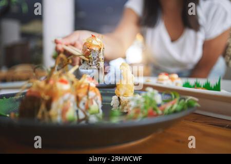 Hand, Nahaufnahme und Essstäbchen im Sushi-Restaurant für Diät, gute Küche und Party mit Catering-Platte. Mensch, gesunder Fisch und Lachs mit Kultur Stockfoto