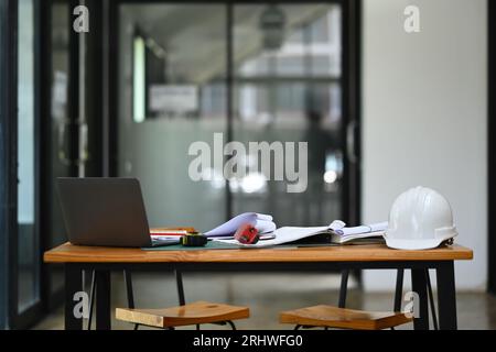 Architect Workstation mit Sicherheitshelmen, Blaupausen und Laptop auf Holztisch. Stockfoto