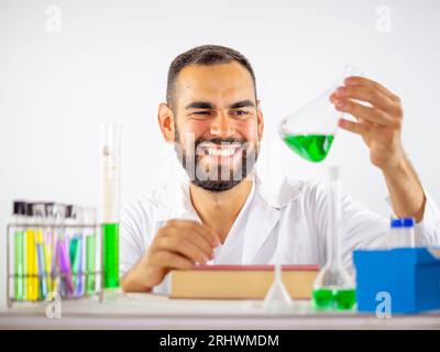 Junger Wissenschaftler beobachtet glücklich eine flüssige Probe in einem erlenmeyerkolben in einem Labor Stockfoto