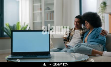 Laptop mit leerem Kopierraum grauer blauer Bildschirm wirbt für Werbevorlagen auf Vordergrundafroamerikanischem Paar Mann Frau zusammen zu Hause Couch Browsing Stockfoto