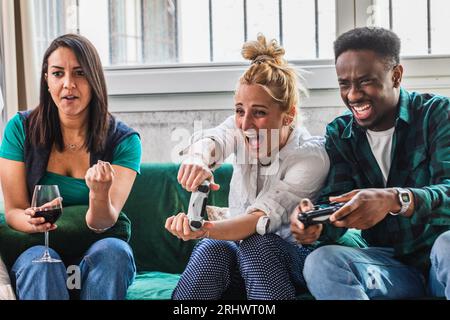 Begeisterte junge Freunde spielen Videospiele. Hitziges Spiel und Gesten der Erregung. Abends zu Hause, Computer und Spielekonsole. Steuerung in h Stockfoto