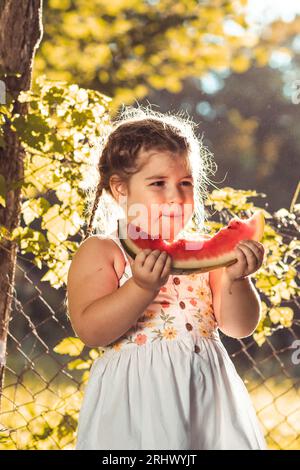 Niedliches kleines Mädchen, das draußen Wassermelone isst Stockfoto