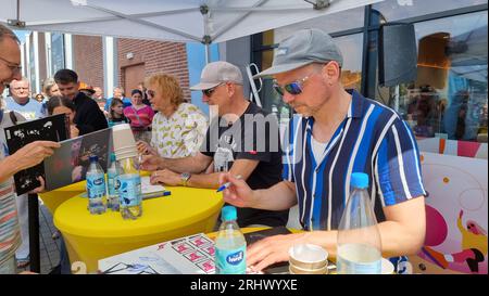 Hannover, Deutschland. August 2023. Christof Stein-Schneider (l-r), Gitarrist, Kai Wingenfelder, Sänger und Christian Decker, Bassist von der Band „Fury in the Smetzhouse“ signiert Autogramme vor dem Zweig einer Drogeriekette. Die sechs Mitglieder der Band "Fury im Schlachthof" sitzen für eine Stunde an der Kasse einer Drogerie für einen guten Zweck. Die Drogerie spendet den gesamten Erlös für die jährliche Weihnachtsfeier für Obdachlose und Bedürftige in Hannover. Quelle: Fernando Martinez/TNN/dpa/Alamy Live News Stockfoto