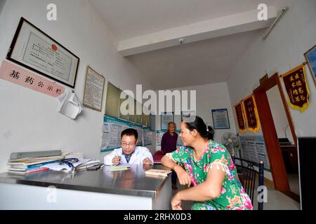 (230819) -- NANCHANG, 19. August 2023 (Xinhua) -- Xiao Jiulin (L) spricht mit einem Patienten in seiner Klinik im Dorf Yangang im Kreis Yudu, ostchinesische Provinz Jiangxi, 15. August 2023. MIT „Funktion: Körperbehinderter Arzt bietet Grundversorgung für Hunderte“ (Xinhua/Hu Chenhuan) Stockfoto