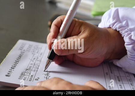 (230819) -- NANCHANG, 19. August 2023 (Xinhua) -- Xiao Jiulin schreibt medizinische Aufzeichnungen für Patienten in seiner Klinik im Dorf Yangang im Kreis Yudu, ostchinesische Provinz Jiangxi, 15. August 2023. MIT „Funktion: Körperbehinderter Arzt bietet Grundversorgung für Hunderte“ (Xinhua/Hu Chenhuan) Stockfoto