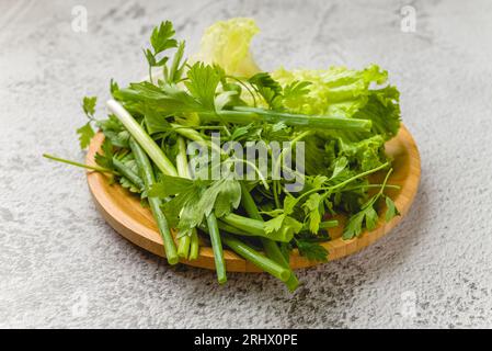 Grüne Bio-Zwiebeln, Schnittlauch, Salat und Petersilie auf einem Steintisch Stockfoto