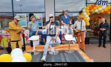 Hannover, Deutschland. August 2023. Gero Drnek (l-r), Keyboarder, Rainer Schumann, Drummer, Kai Wingenfelder, Sänger Christian Decker, Bassist, und Christof Stein-Schneider, Gitarrist, von der Band „Fury in the Shatterhouse“ treten vor dem Zweig einer Drogeriekette auf. Die sechs Mitglieder der Band "Fury im Schlachthof" sitzen für eine Stunde an der Kasse einer Drogerie für einen guten Zweck. Die Drogerie spendet den gesamten Erlös für die jährliche Weihnachtsfeier für Obdachlose und Bedürftige in Hannover. Quelle: Fernando Martinez/TNN/dpa/Alamy Live News Stockfoto