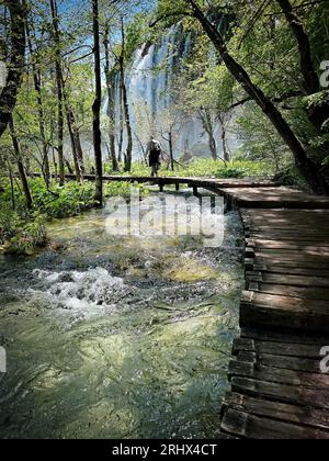 Ein Wanderer nähert sich den Gewässern, die über die Felsvorsprünge der oberen Seen im Plitvicer Nationalpark, Kroatien, fließen. Stockfoto