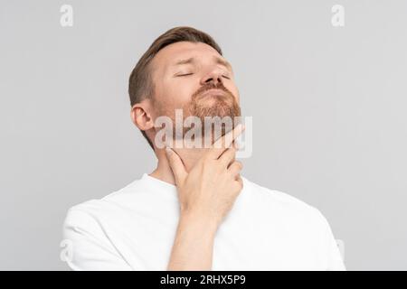 Der Mann hält sich am Hals fest und leidet an Halsschmerzen. Erkältung, Krankheit. Isoliert auf grauem Hintergrund Stockfoto