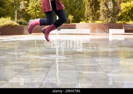 Glückliche Frau mit Stiefeln springt in einer Regenpfütze Stockfoto