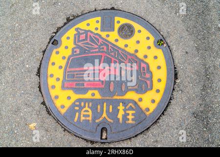 Japanischer, monochromatischer Schachtdeckel aus Stahl. In Gelb und Rot gehalten, mit einer Feuerwehrauto der Feuerwehr von Kumamoto. Stockfoto