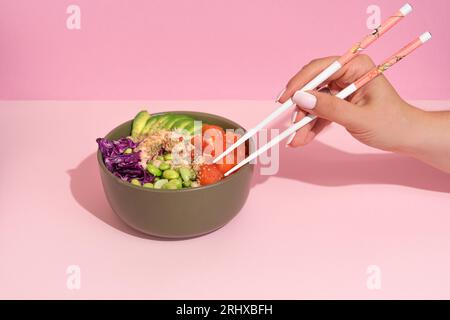 Hände essen Poke Bowl mit Lachs auf rosafarbenem Hintergrund Stockfoto